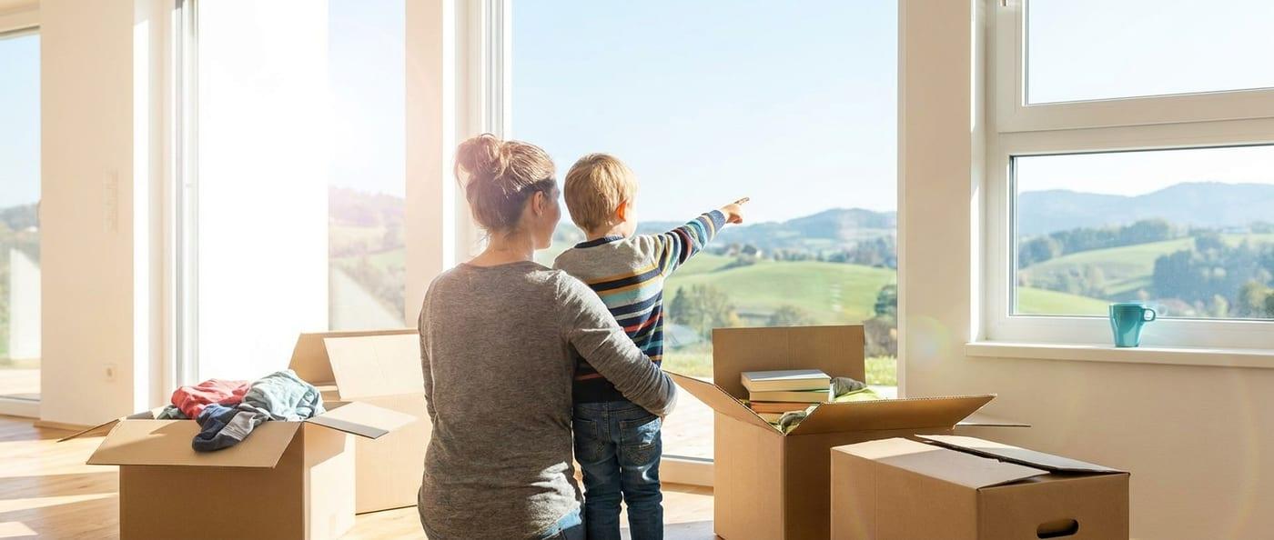 Eltern und Kind sitzen zwischen Umzugskartons am Fenster der neuen Wohnung nach dem Einzug