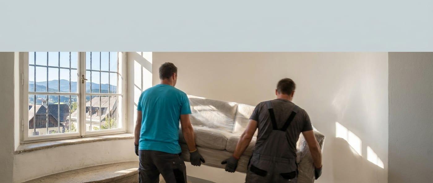 Zwei Umzugshelfer von SpeedTransport tragen ein verpacktes Sofa durch ein Stiegenhaus